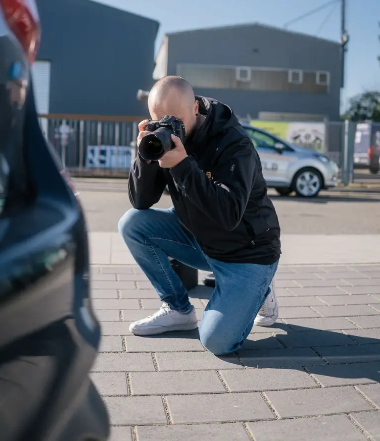 Kfz-Gutachter kniet am Fahrzeug und fotografiert einen Karosserieschaden