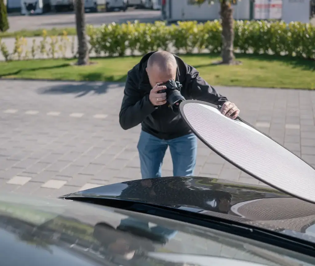 Kfz-Gutachter fotografiert Lackschaden mit Kamera und Reflektor