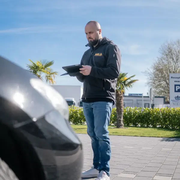 Kfz-Gutachter bei der Schadensaufnahme mit Tablet vor einem Fahrzeug
